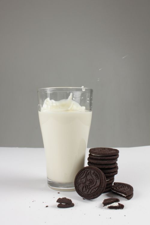 a picture of a small milk spash with oreo cookies by the glass of milk